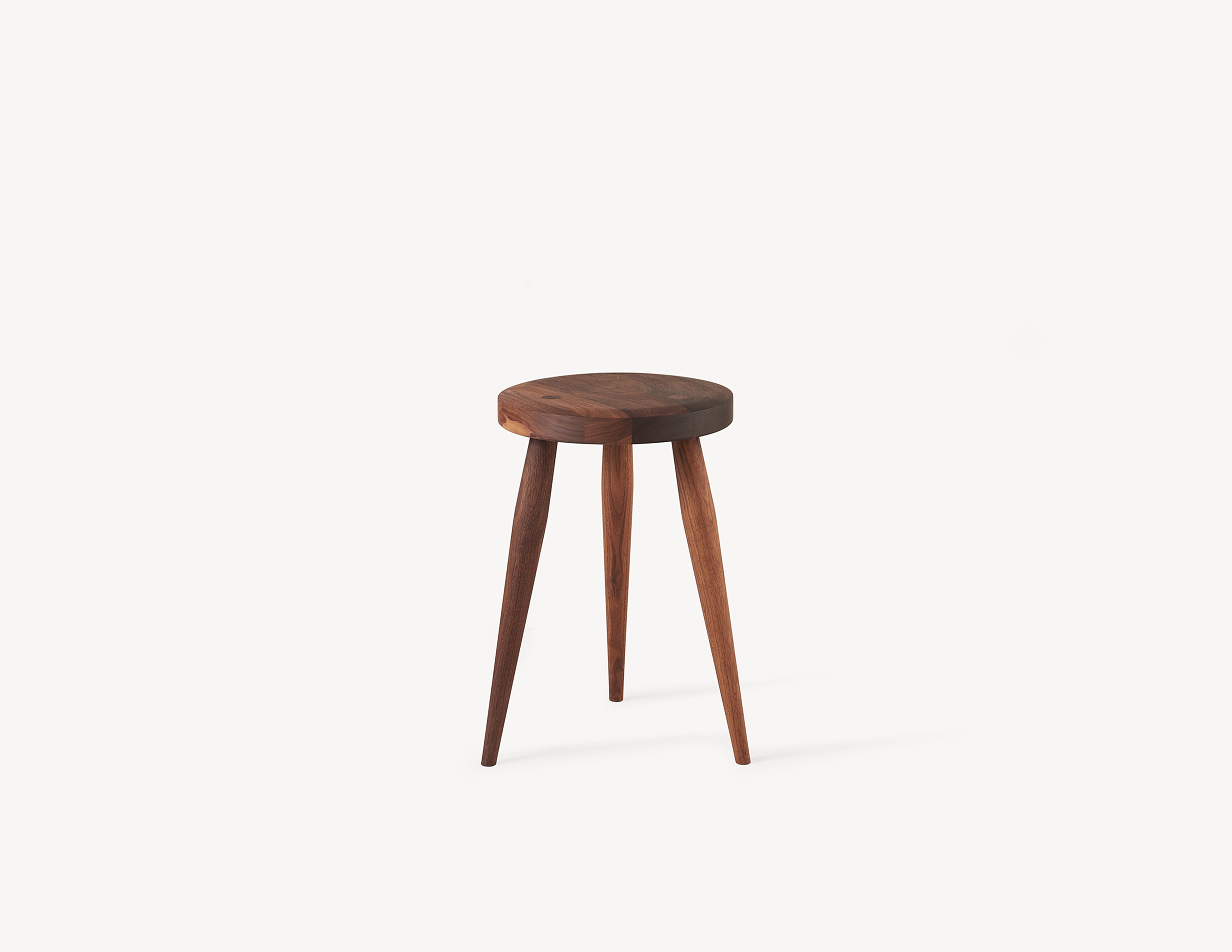 Three-legged brown milking stool with turned legs and circular seat in black walnut wood