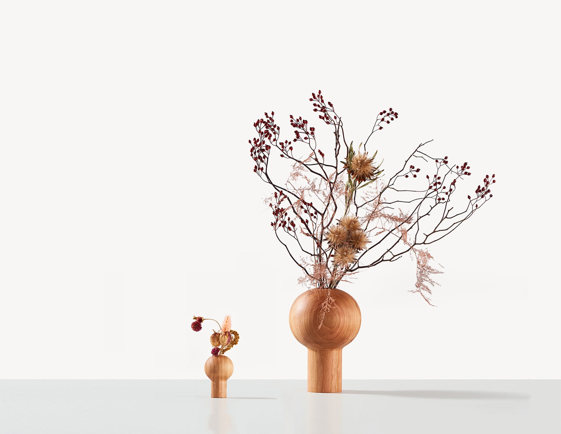 two round wood dry vases in cherry wood, with Ikebana flower arrangements.