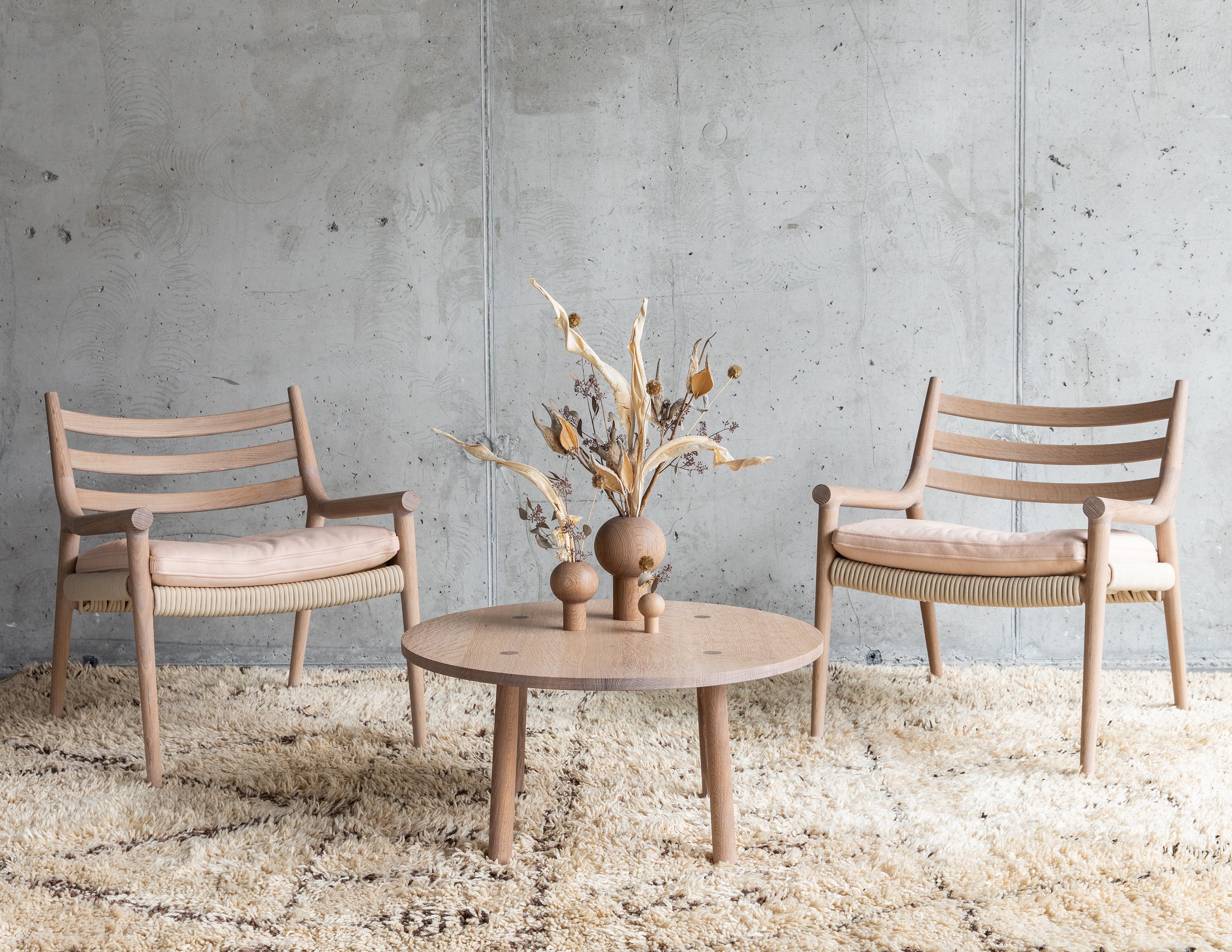 two light wood oak lounge chairs, a light wood oak coffee table, and three round light wood oak dry vases, with Ikebana flower arrangements.