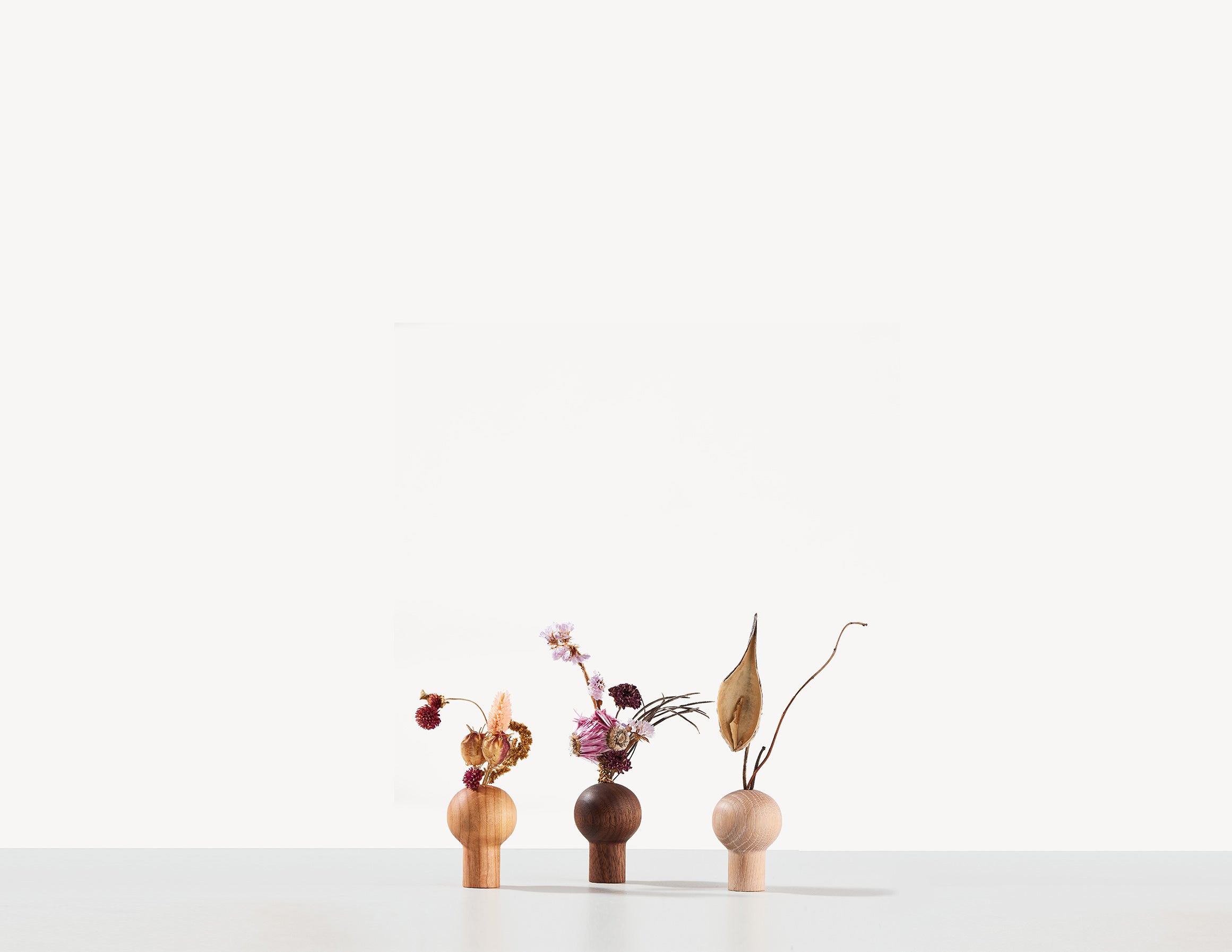 three small round wooden dry vases in a row, with Ikebana flower arrangements.